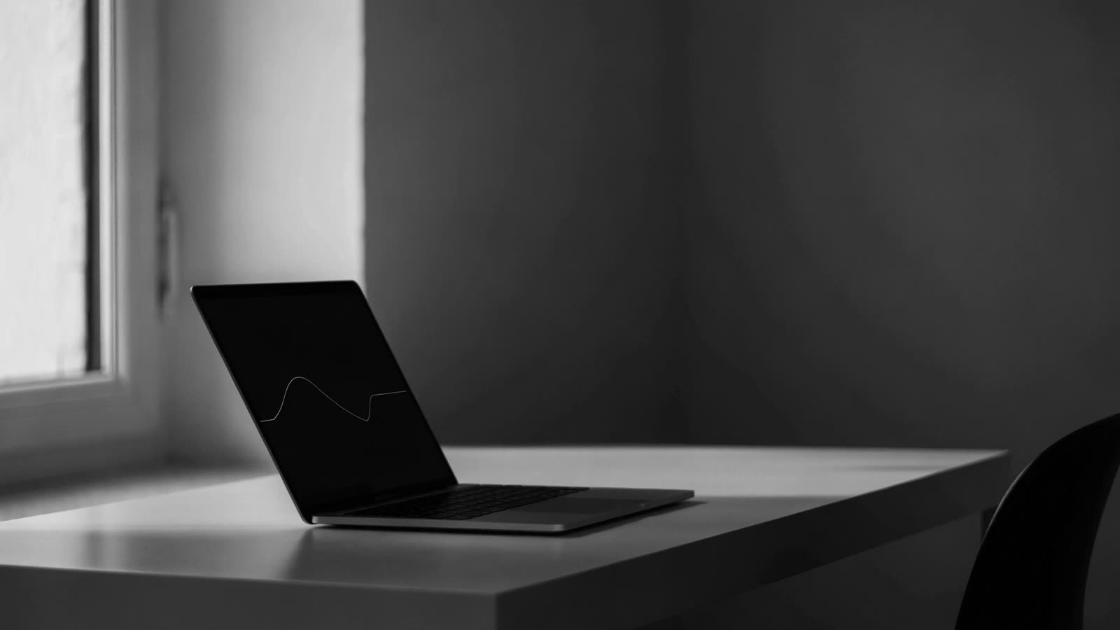 Notebook aberto numa mesa clara junto à janela, com uma curva simples na tela escura