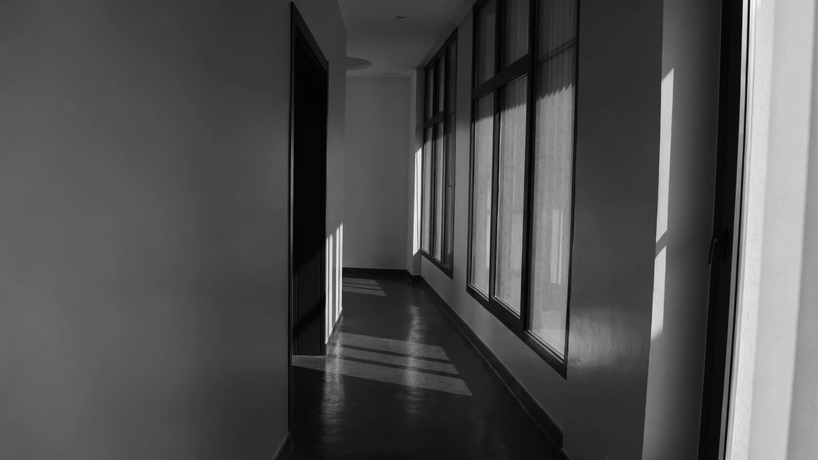 Corredor de clínica vazio, com janelas à direita e faixas de luz no piso